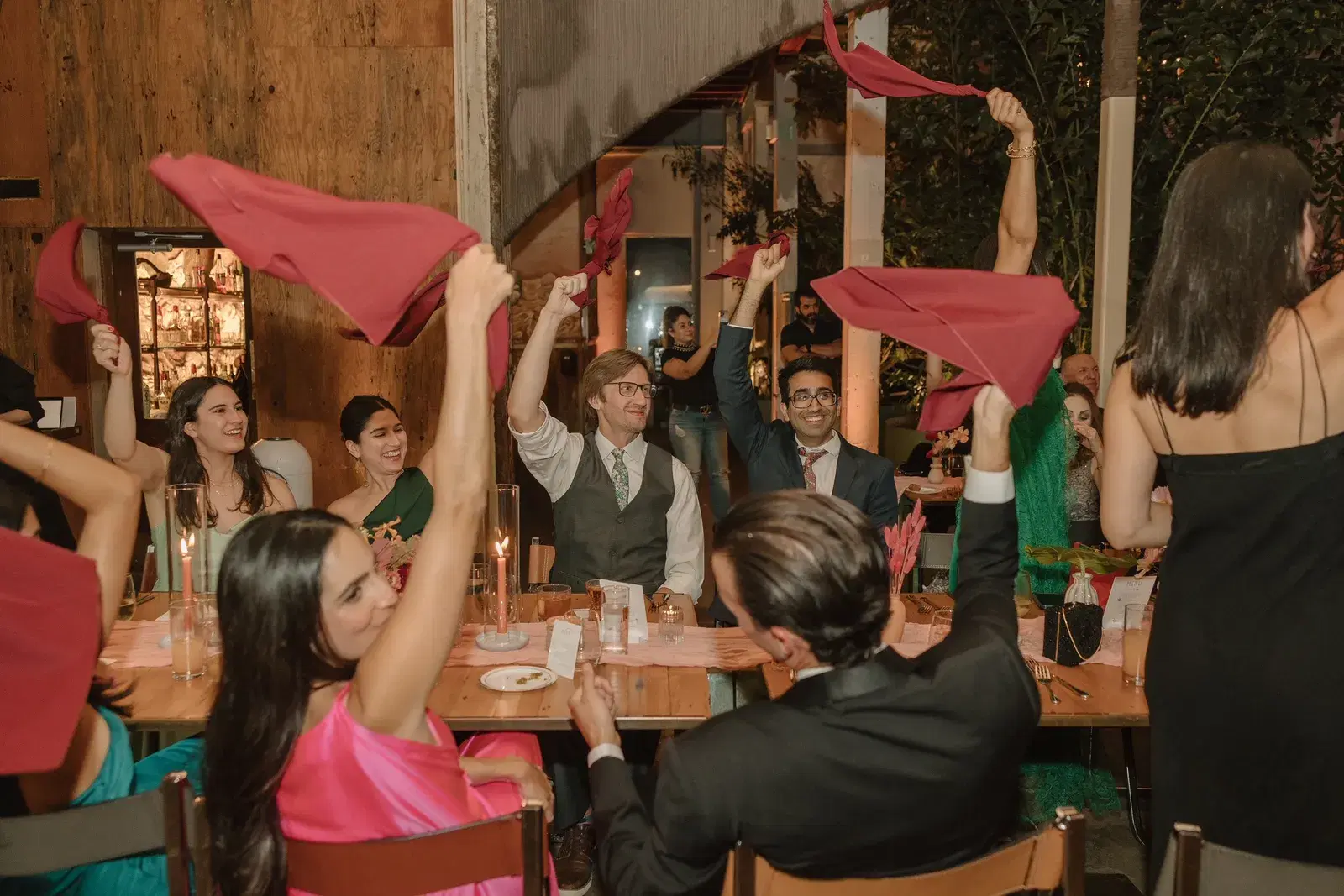 Wedding guests waving red napkins overhead at their dinner tables during a lively reception moment
