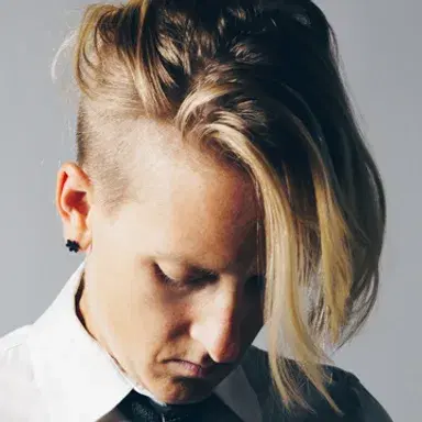 Portrait of DJ Danni Ammon in a white shirt and black tie, head lowered