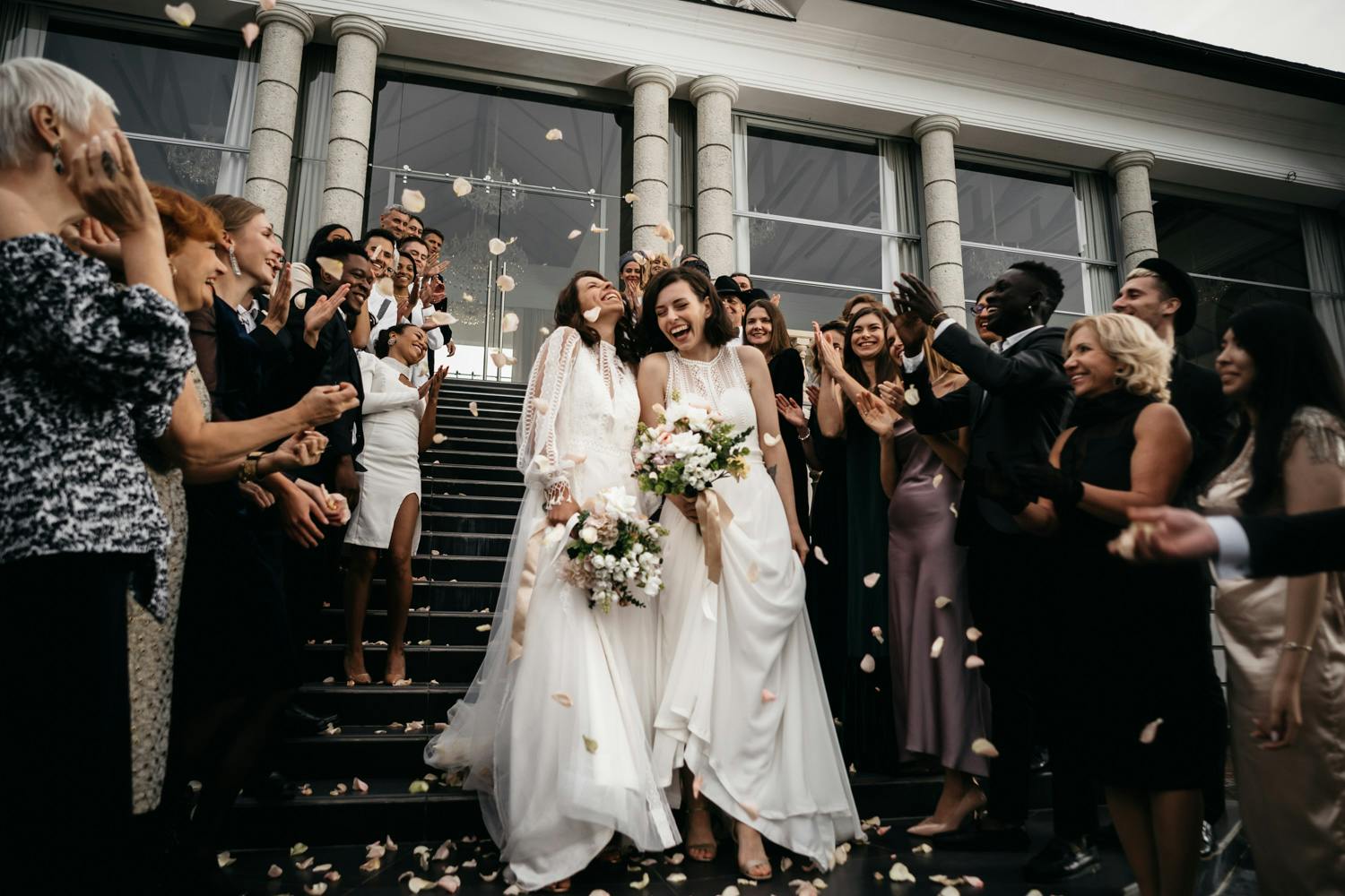 Two brides exit church excited after their wedding, guests smile and cheer for them