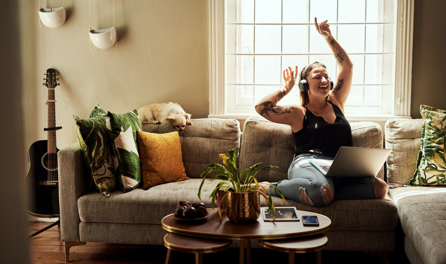 Curvy white woman with her hands up smiling sitting on her couch with her laptop